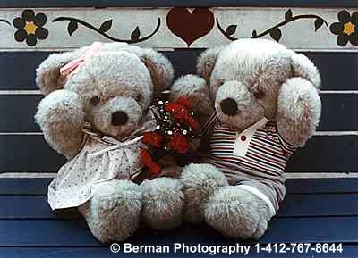 Teddy Bear couple celebrating their love with flower sitting on a bench